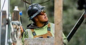 Construction worker in a hard hat and safety glasses at a construction site, looking up.